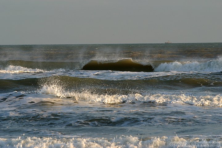 waves breaking in to an onshore breeze with a ship in the distance