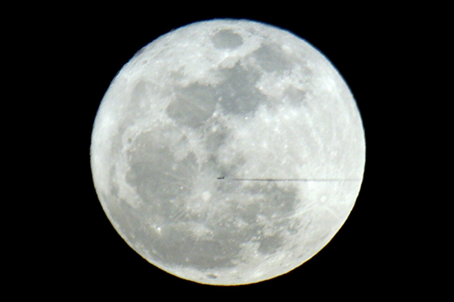 a jet and contrail silhouetted against the moon